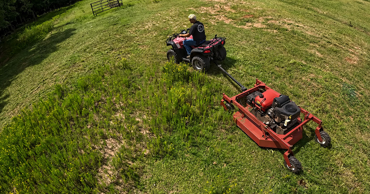 Cook&rsquo;s BrushRipper tow-behind brush cutter clearing an overgrown field behind an ATV