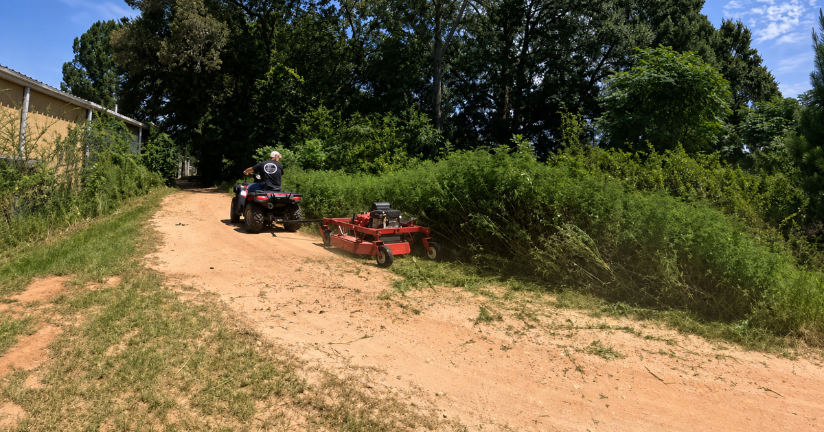 Tow-behind brush mower clearing thick growth along a rural field edge